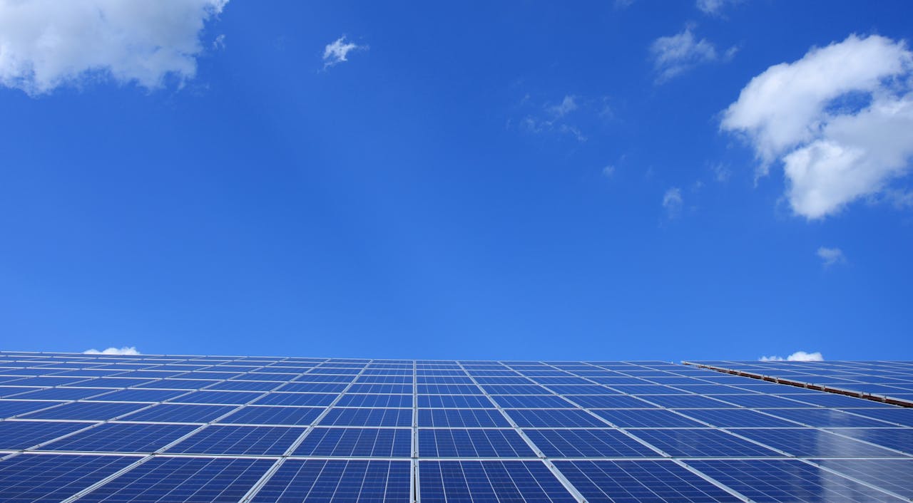 home-hero A low angle view of solar panels under a bright blue sky with clouds.